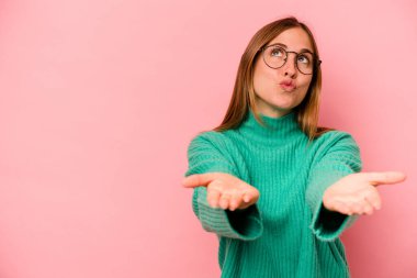 Beyaz bir kadın pembe arka planda izole edilmiş dudaklar kıvrılmış ve hava öpücüğü göndermek için avuç içleri tutulmuş..