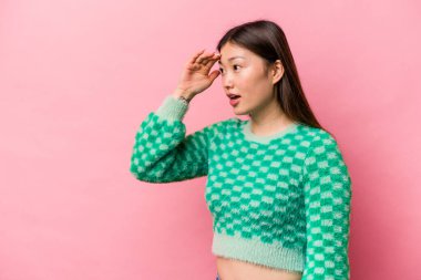 Pembe arka planda izole edilmiş genç Çinli kadın uzaklara bakıyor ve elini alnına koyuyor..