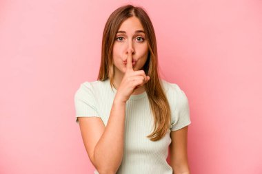 Pembe arka planda izole edilmiş genç beyaz kadın ya sır saklıyor ya da sessizlik istiyor..