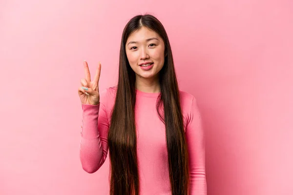 年轻的中国女人在粉红的背景上孤立无援 快乐而无忧无虑 用手指展示和平的象征 — 图库照片