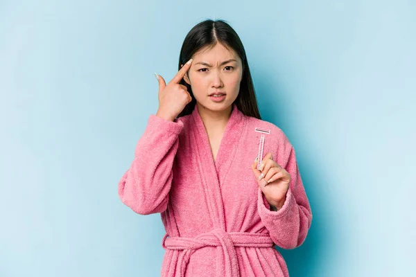 年轻的亚洲女人拿着被蓝色背景隔离的剃须刀片 用食指表示失望的姿态 — 图库照片