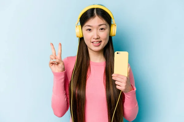 Jovem Mulher Asiática Ouvindo Música Isolada Fundo Azul Mostrando Número — Fotografia de Stock