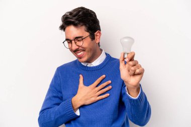 Beyaz arka planda izole edilmiş ampul tutan genç beyaz bir adam gülüyor ve eğleniyor..