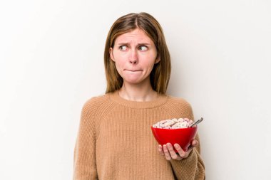 Beyaz arka planda izole edilmiş mısır gevreği yiyen genç İngiliz kadın kafası karışmış, kuşkulu ve kararsız hissediyor.