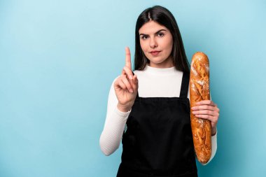 Genç fırıncı Kafkas elinde bir somun ekmek tutarken mavi arka planda bir numarayı parmağıyla gösteriyor..