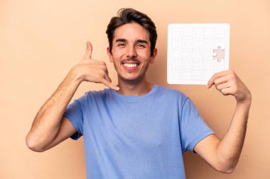 Elinde bej arka planda izole edilmiş bir yapboz tutan genç beyaz bir adam parmakları olan bir cep telefonu hareketi gösteriyor..