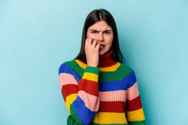 Mavi arka planda izole edilmiş, tırnak yiyen, gergin ve endişeli bir beyaz kadın..