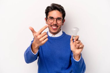 Beyaz arka planda izole edilmiş bir ampul tutan genç beyaz bir adam seni işaret ediyor. Sanki davet ediliyormuş gibi..