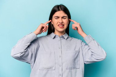 Genç beyaz kadın mavi arka planda izole edilmiş parmaklarıyla kulaklarını kapatıyor, gürültülü bir ortam yüzünden stresli ve çaresiz..