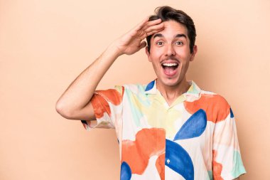 Beyaz tenli genç adam bej arka planda izole edilmiş yüksek sesle bağırıyor, gözleri açık ve elleri gergin tutuyor..