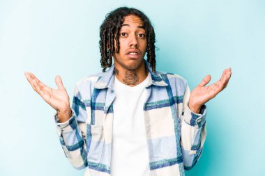 Genç Afrikalı Amerikalı bir adam mavi arka planda izole edilmiş. Şaşırmış ve şok olmuş..