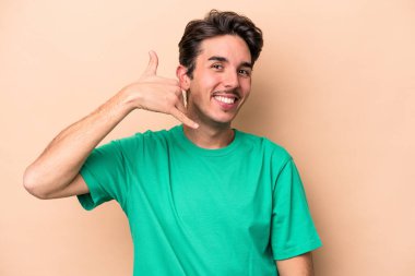 Beyazlı genç bir adam bej arka planda izole edilmiş. Cep telefonu hareketini parmaklarıyla gösteriyor..