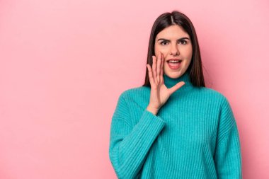 Pembe arka planda izole edilmiş genç beyaz kadın yüksek sesle bağırıyor, gözleri açık ve elleri gergin tutuyor..