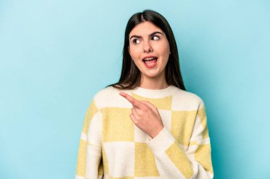 Mavi arka planda soyutlanmış genç beyaz kadın gülümseyen, neşeli ve keyifli bir tarafa bakıyor..