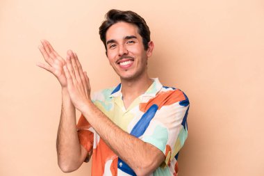 Beyaz tenli genç adam bej arka planda izole edilmiş enerjik ve rahat hissediyor, ellerini ovuşturuyor kendinden emin..