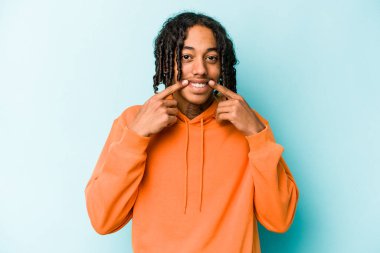 Genç Afrikalı Amerikalı adam mavi arka planda izole edilmiş gülümsüyor, parmaklarını ağıza doğrultuyor..