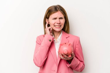 Genç İngiliz kadın kumbarasını tutuyor. Beyaz arka planda izole edilmiş. Kulakları elleriyle kapatıyor..