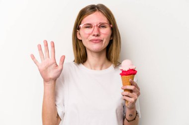 Beyaz arka planda izole edilmiş dondurmayı tutan genç İngiliz kadın gülümseyerek beş numarayı parmaklarıyla gösteriyor..