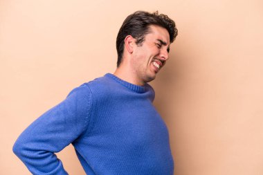 Bej arka planda izole edilmiş beyaz bir adam sırt ağrısı çekiyor..