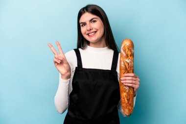 Genç fırıncı Kafkas elinde mavi arka planda izole edilmiş bir somun ekmek tutuyor neşeli ve kaygısız parmaklarıyla barış sembolü gösteriyor.