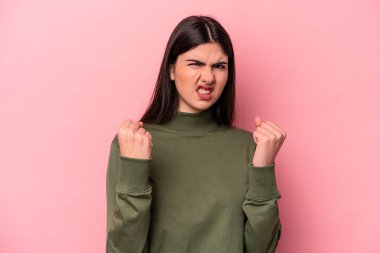 Pembe arka planda izole edilmiş genç beyaz kadın yumruğunu kameraya gösteriyor, agresif yüz ifadesi..