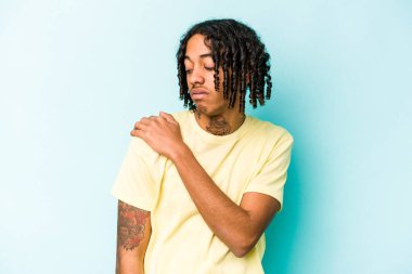 Genç Afrikalı Amerikalı bir adam mavi arka planda izole edilmiş, omuz ağrısı var..