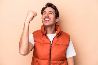 Beyazlı genç adam bej arka planda izole edilmiş zafer, tutku ve coşkuyu kutluyor, mutlu bir ifade..