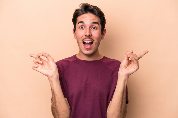 Молодой кавказский человек выделяется на бежевом фоне, указывая на разные копировальные пространства, выбирая одно из них, показывая пальцем.