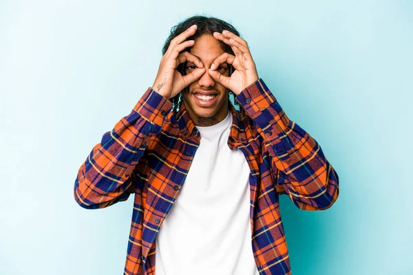 Genç Afro-Amerikalı adam mavi arka planda izole edilmiş, gözlerinde sorun yok işareti var.