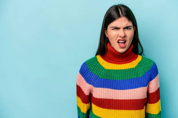 Kafkasyalı genç bir kadın mavi arka planda izole edilmiş çok kızgın, öfkeli, hayal kırıklığına uğramış bağırıyor..