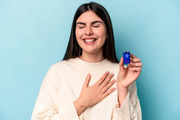 Ung Kaukasisk Kvinna Håller Ett Batteri Isolerad Blå Bakgrund Skrattar — Stockfoto