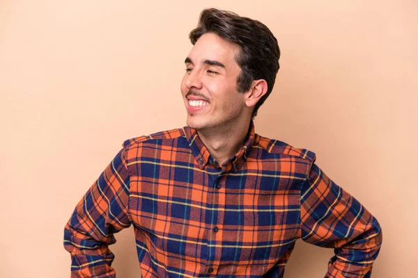 Beyaz tenli genç adam bej arka planda izole edilmiş. Kendine güveniyor. Kalçaları tutuyor..