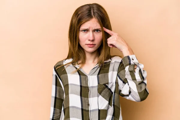 Young English woman isolated on beige background pointing temple with finger, thinking, focused on a task.