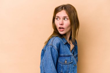 Bej arka planda soyutlanmış genç bir İngiliz kadın gülümseyen, neşeli ve hoş bir kenara bakıyor..