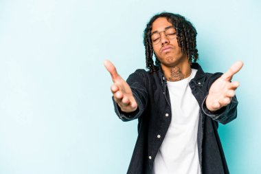 Genç Afrikalı Amerikalı adam mavi arka planda izole edilmiş dudaklarını kıvırıyor ve hava öpücüğü göndermek için avuç içi tutuyor..