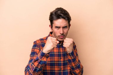 Beyazlı genç bir adam bej arka planda izole edilmiş, yumruğunu kameraya gösteriyor, agresif yüz ifadesi var..