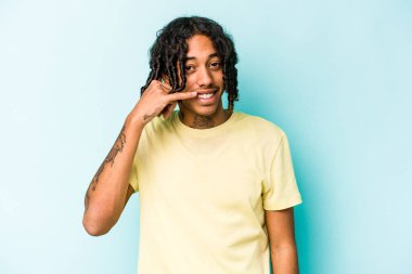 Genç Afrikalı Amerikalı bir adam mavi arka planda izole edilmiş, parmakları olan bir cep telefonu hareketi gösteriyor..