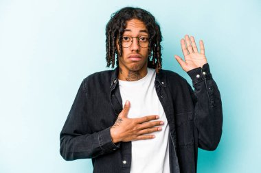 Genç Afrikalı Amerikalı adam mavi arka planda izole edilmiş bir şekilde yemin ediyor, elini göğsüne koyuyor..