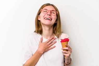 Beyaz arka planda izole edilmiş dondurmayı tutan genç bir İngiliz kadın elini göğsünde tutarak kahkahalar atıyor..