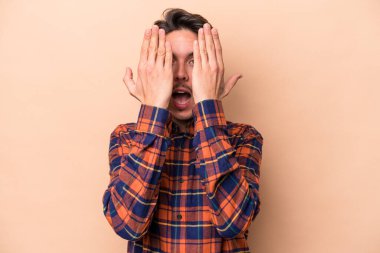 Beyaz tenli genç adam bej arka planda izole edilmiş. Yüzünün yarısını palmiye ile örterek eğleniyor..