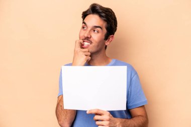 Beyazlı genç bir adam bej arka planda izole edilmiş bir levha tutuyor. Bir şeyin fotokopi odasına baktığını düşünüyor..