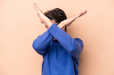 Beyazlı genç adam bej arka planda izole edilmiş iki kolu çapraz tutuyor, inkar kavramı.