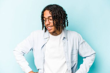 Mavi arka planda izole edilmiş genç Afrikalı Amerikalı adam mutlu bir şekilde gülüyor ve ellerini karnının üstünde tutarak eğleniyor..