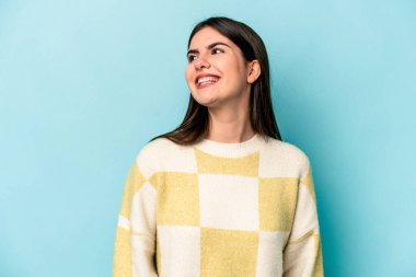 Genç beyaz kadın mavi arka planda izole edilmiş rahat ve mutlu bir şekilde gülüyor, boynunda dişlerini gösteriyor..