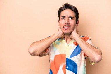 Kafkasyalı genç adam bej arka planda izole edilmiş kafasının arkasına dokunuyor, düşünüyor ve bir seçim yapıyor..