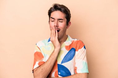 Beyazlı genç bir adam bej arka planda izole edilmiş esniyor. Ağzı eliyle kapatan yorgun bir hareket sergiliyor..