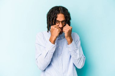 Genç Afrikalı Amerikalı bir adam mavi arka planda izole edilmiş. Bir tartışma yüzünden yumruk, öfke ve kavga atıyor..