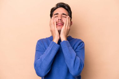 Beyaz tenli genç adam bej arka planda izole edilmiş ağlıyordu, bir şeyden mutsuzdu, ıstırap ve kafa karışıklığı vardı..