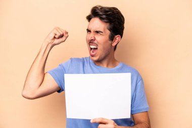 Beyazlı genç adam bej arka planda izole edilmiş bir plaket tutuyor zafer kazandıktan sonra yumruğunu kaldırıyor, kazanan konsept..