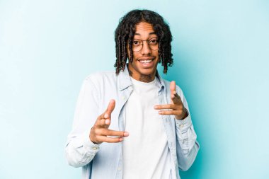 Genç Afro-Amerikalı adam mavi arka planda izole edildi. Neşeli gülümsemeler ön tarafı işaret ediyor..